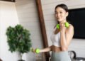 Active and healthy asian girl with fit body doing fitness exercises at home, lifting dumbbells and smiling, workout in living room.
